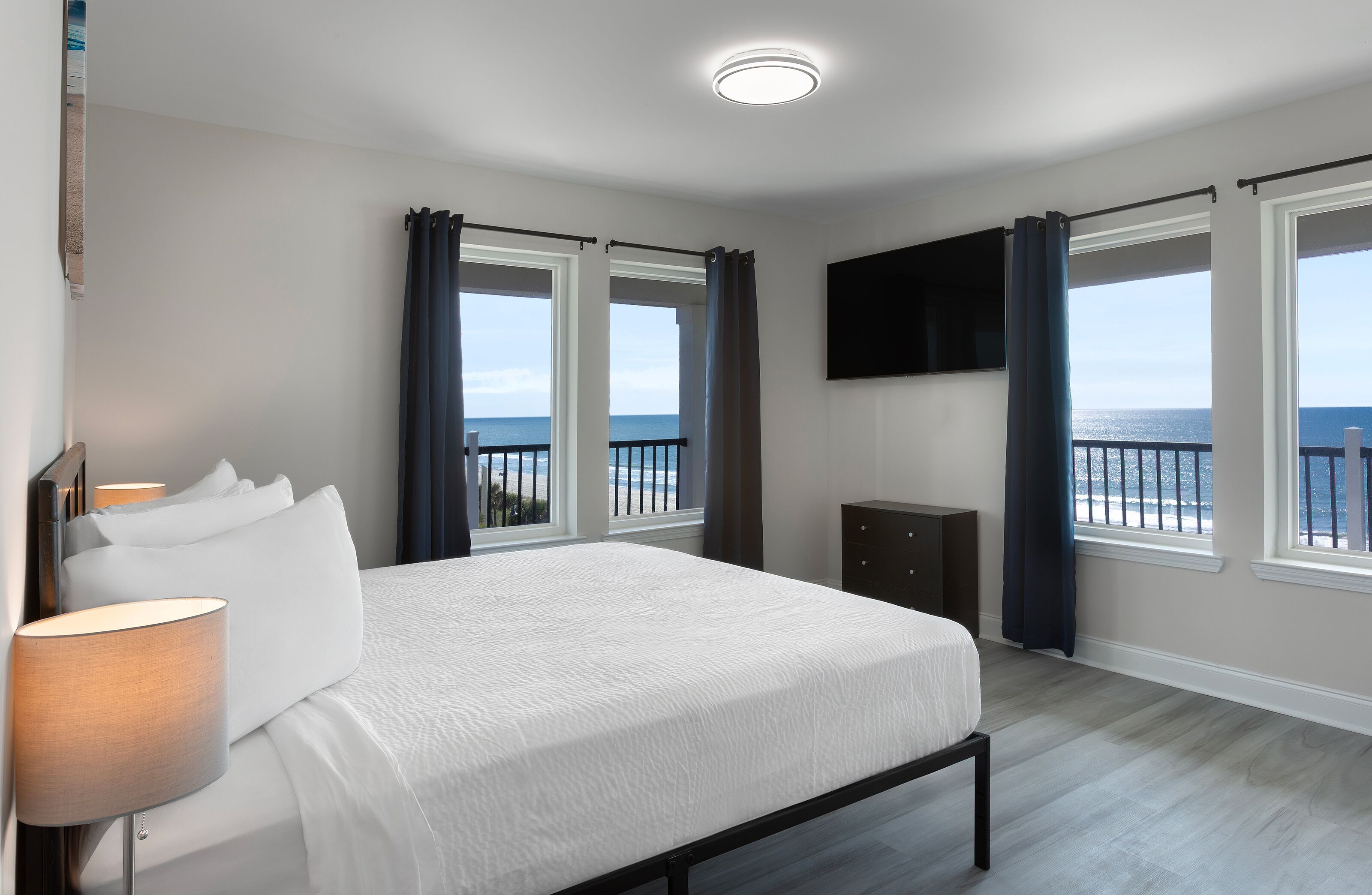 A bedroom with a bed, a TV mounted on the wall, and windows with curtains.