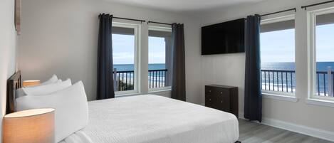 A bedroom with a bed, a TV mounted on the wall, and windows with curtains.