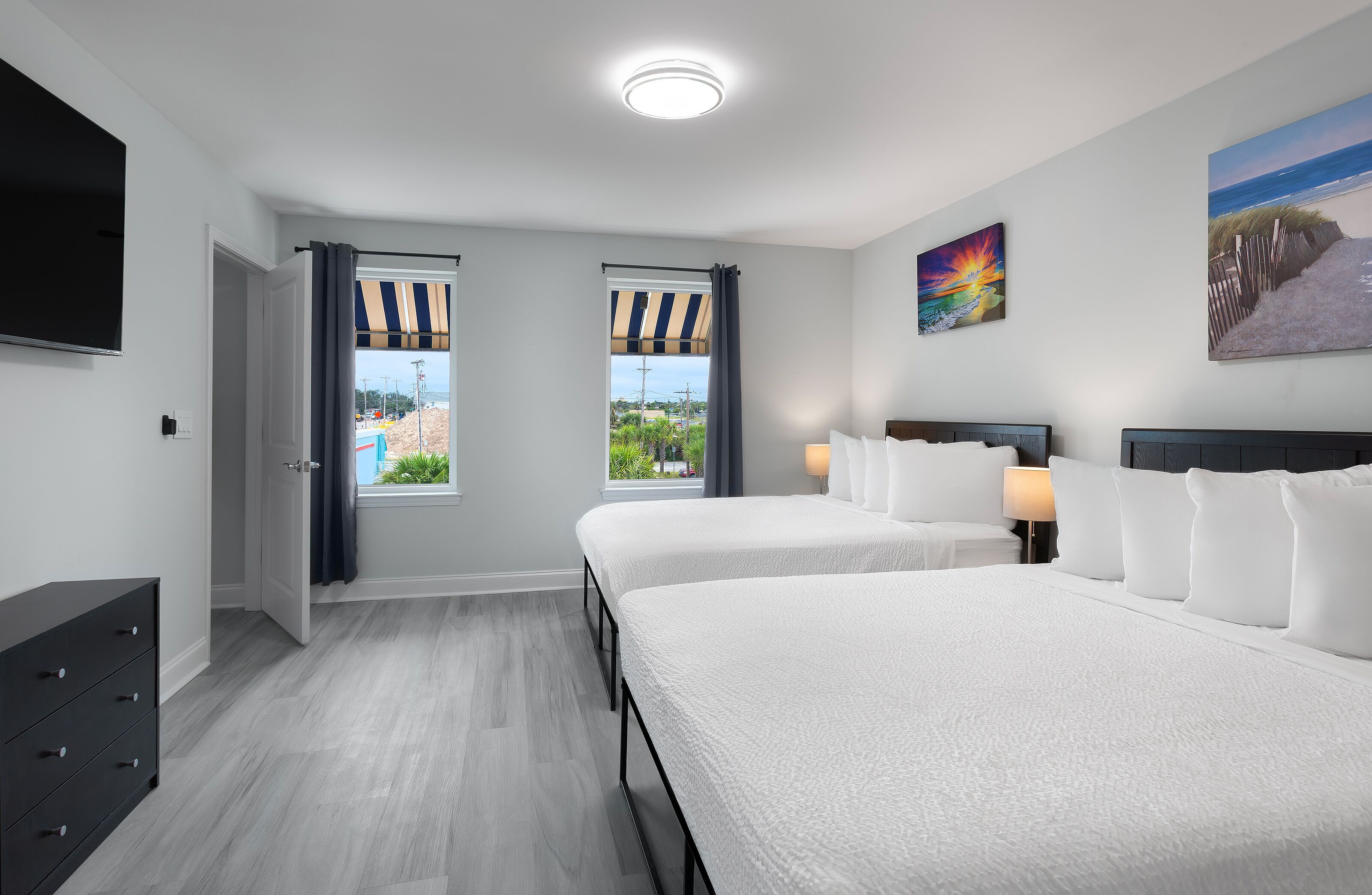 A hotel room with two beds, a TV, a window with curtains, and a painting on the wall.