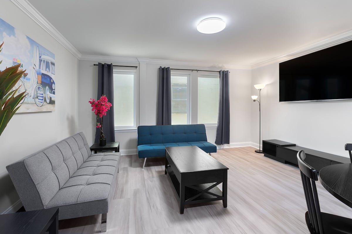 A modern living room with a grey sofa, a blue sofa, a black coffee table, and a TV on the wall.