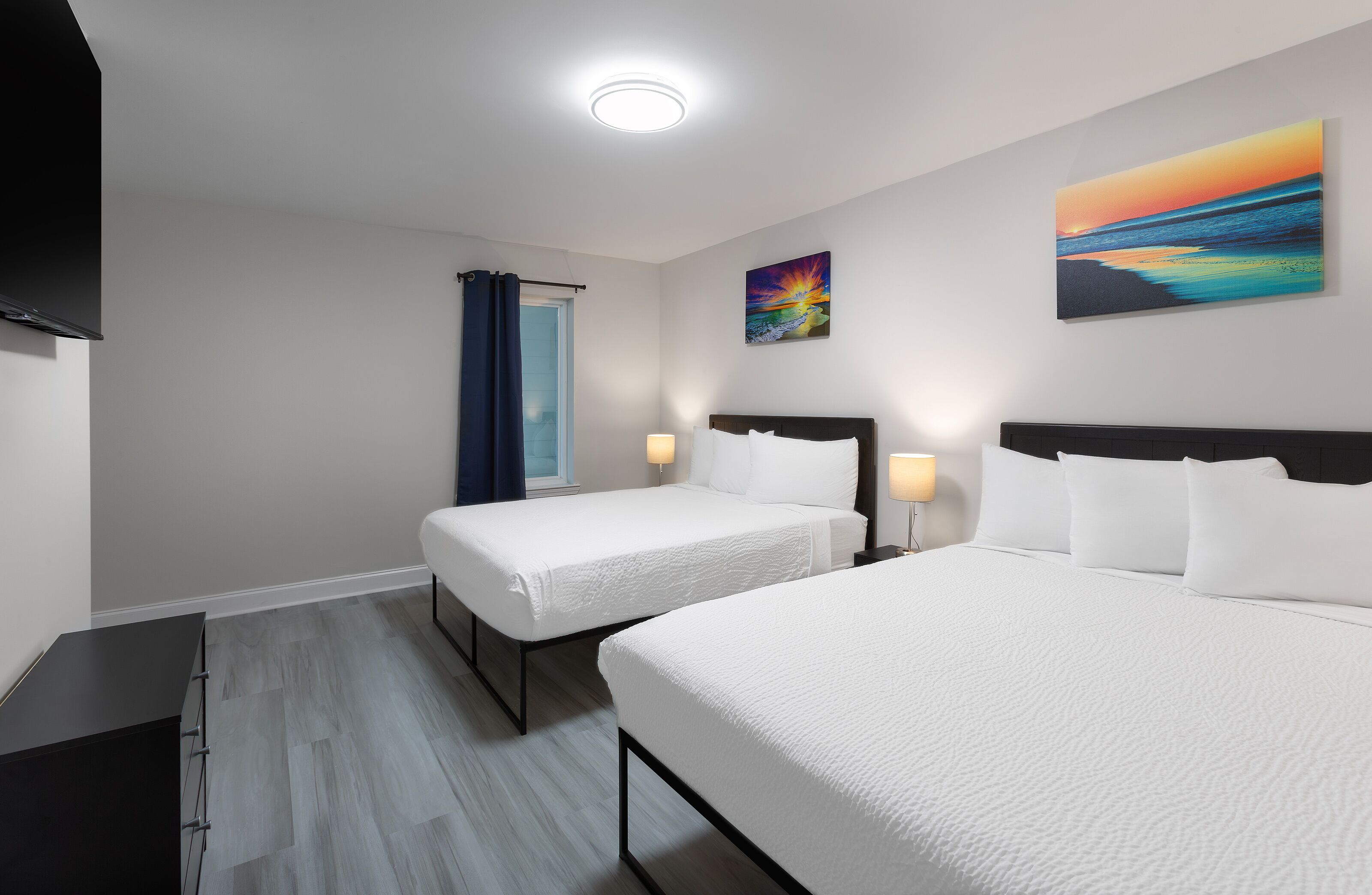 Quarto de hotel com duas camas, televisão, quadro e janela com cortinas.