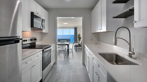 A modern kitchen with white cabinetry, stainless steel appliances, and a view to the outside. - Ocean Escape Boardwalk Oceanfront  (Myrtle Beach)