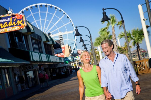 A boardwalk with shops and a Ferris wheel in the background.