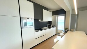 Een moderne keuken met witte kasten, een inbouwoven en een groot raam met uitzicht op zee.