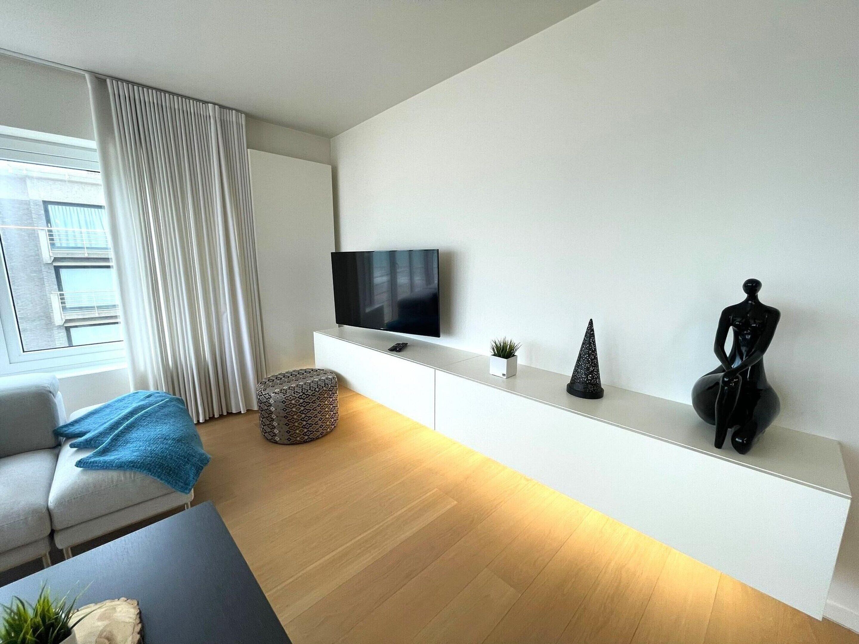 A modern living room with a flat-screen TV, a sofa, a coffee table, and a decorative sculpture.