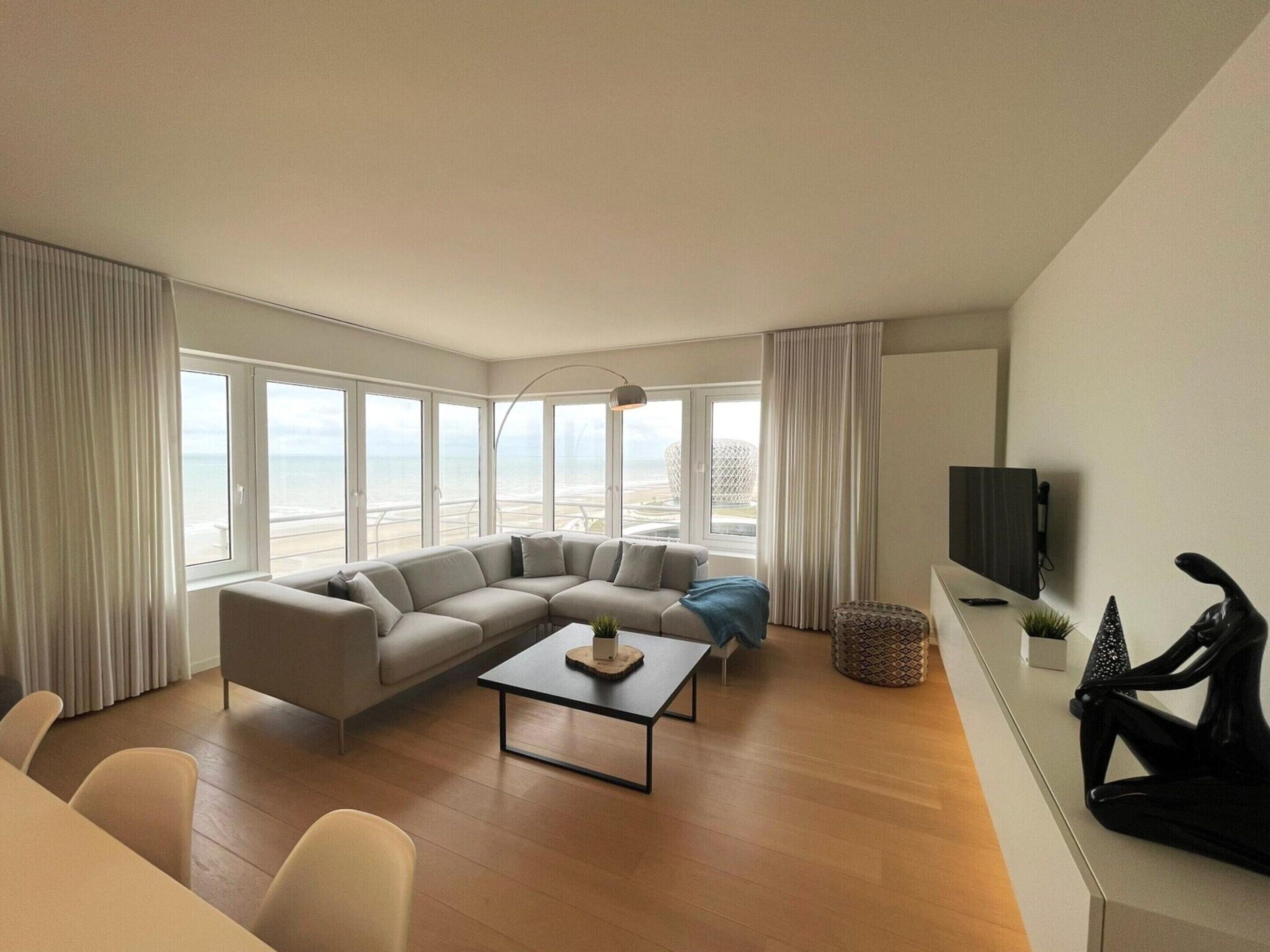 A modern living room with a large L-shaped sofa, a coffee table, and a TV on a stand.