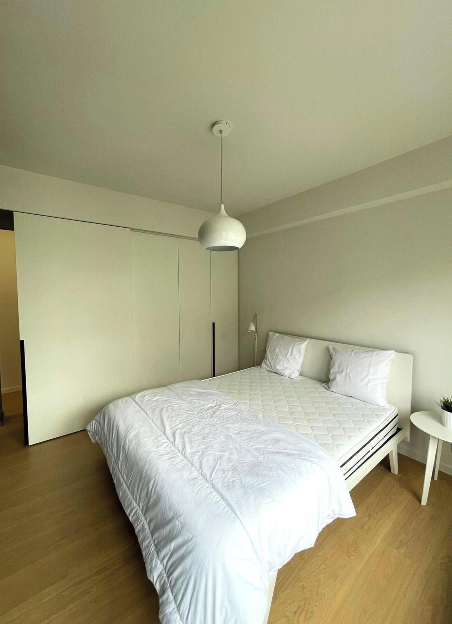 A modern bedroom with a large bed, a white wardrobe, and a small bedside table.