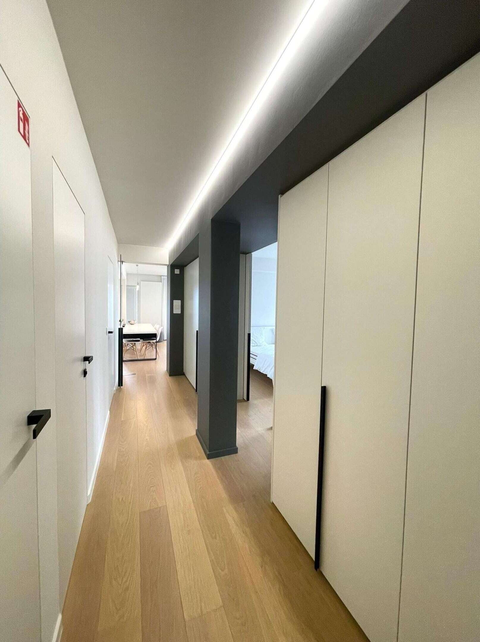 A modern hotel corridor with wooden flooring, white walls, and a dark accent wall.