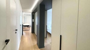 Een moderne hotelgang met houten vloer, witte wanden en een donkere accentmuur.
