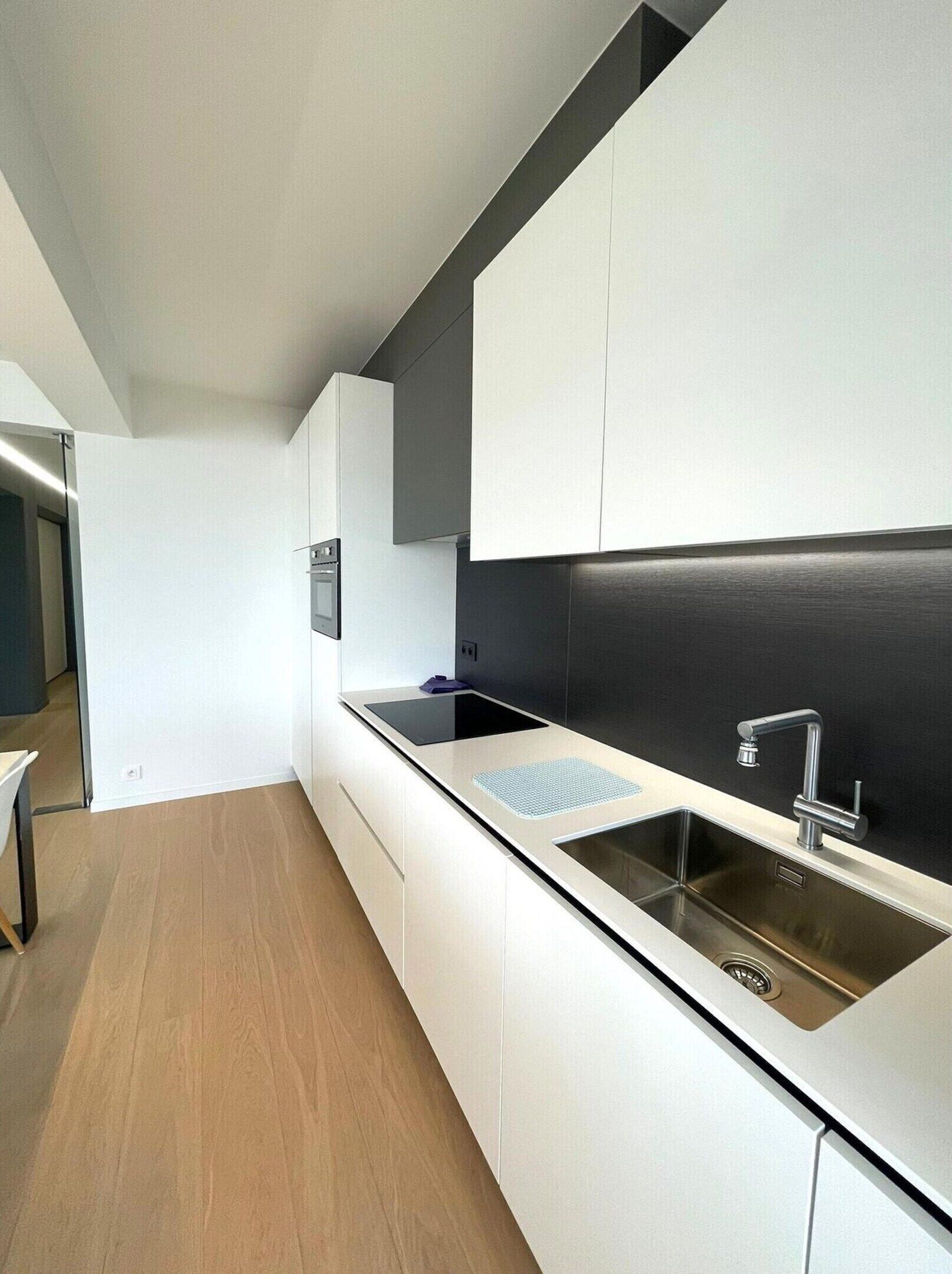 Una cucina moderna con mobili bianchi, una parete di sfondo nera e un lavello in acciaio inossidabile.