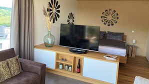 Una sala de estar moderna con televisor, muebles de madera, detalles decorativos en la pared y vista a zonas verdes.