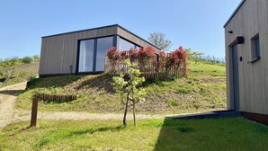 Un edificio moderno con un amplio ventanal, una valla de madera con flores rojas y una zona cubierta de césped.