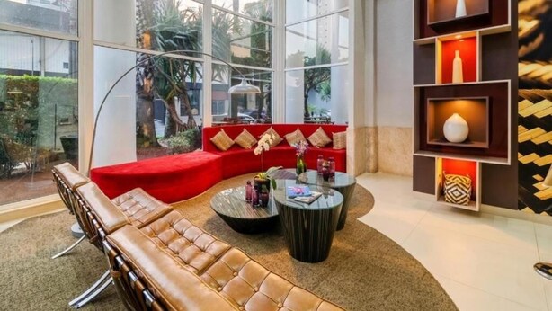 Un área de descanso moderna con sofás de cuero, una mesa de centro de vidrio y una estantería decorativa con jarrones.