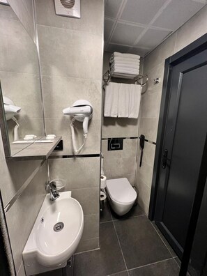 Um banheiro moderno com pia, secador de cabelo, vaso sanitário e porta-toalhas.
