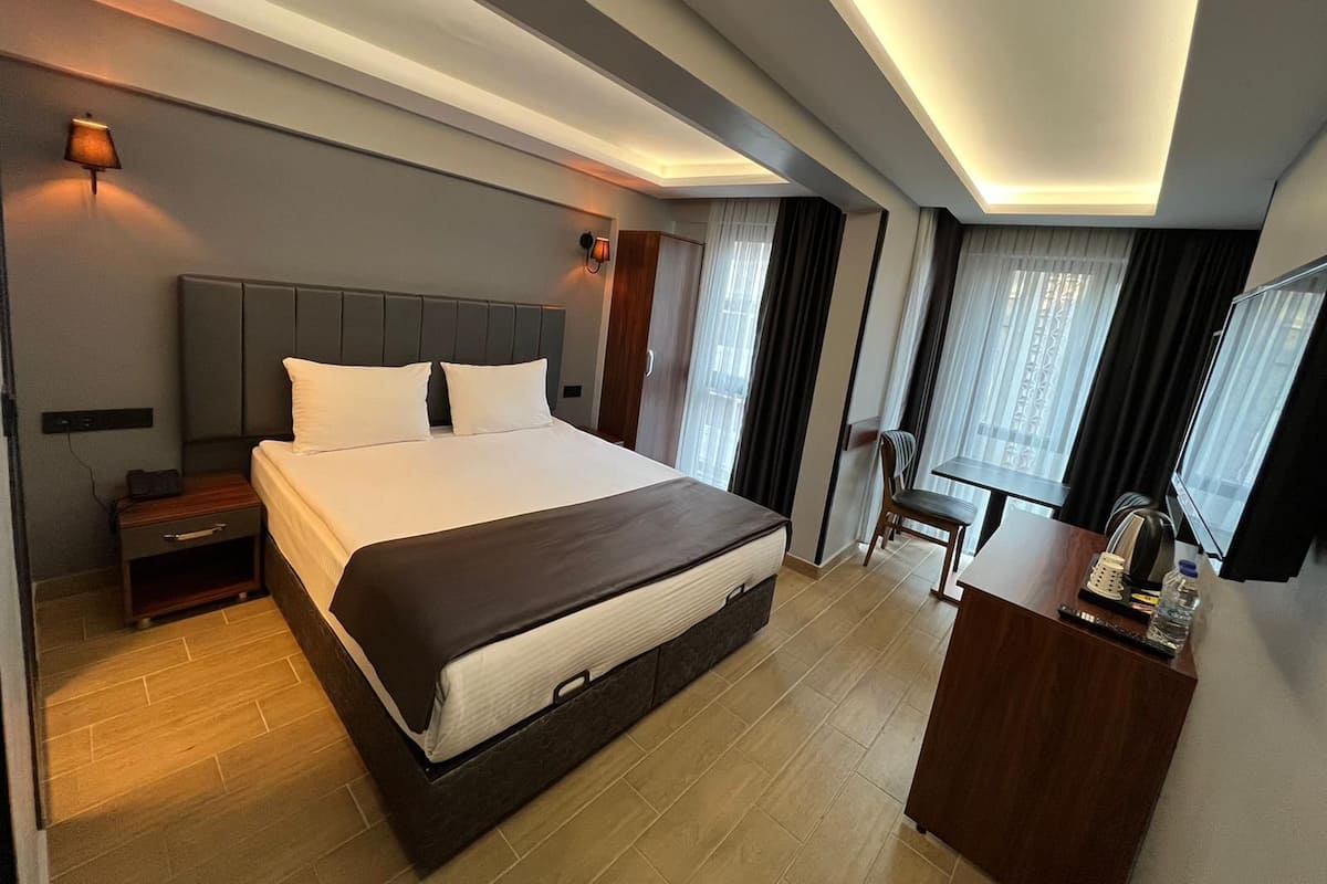 A modern hotel room with a large bed, bedside tables, a desk with a chair, and a TV.
