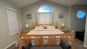 Une chambre à coucher comprenant un lit, un banc, un ventilateur de plafond, une fenêtre et une petite lucarne.