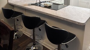 Une cuisine moderne avec un plan de travail en marbre, trois tabourets de bar noirs, un four à micro-ondes et un panneau décoratif représentant le mot « HOME » accroché au mur.