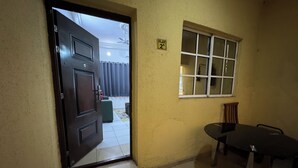 Une porte ouverte donne sur une pièce avec une fenêtre, une petite table et une chaise.