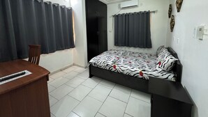 Une chambre à coucher comprenant un lit, un bureau, une chaise, un ventilateur de plafond et une porte.
