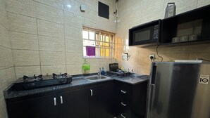 Une cuisine équipée d’une cuisinière à gaz, d’un évier, de meubles de rangement noirs, d’un réfrigérateur en acier inoxydable et d’un four à micro-ondes placé au-dessus du plan de travail.