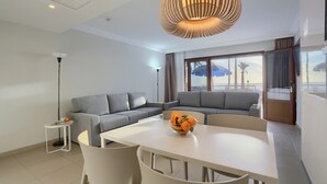 A modern living room with a grey sectional sofa, a dining table with chairs, a small side table, and a large window with a view of the beach. - Playa Flamingo  Margarita (Playa Blanca)