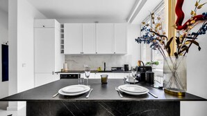 Uma cozinha moderna com armários brancos, painel de parede de mármore e uma ilha de mármore preta com dois pratos e copos brancos.