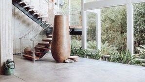 Un intérieur moderne avec un escalier, un grand vase et une vue sur la verdure à l’extérieur.
