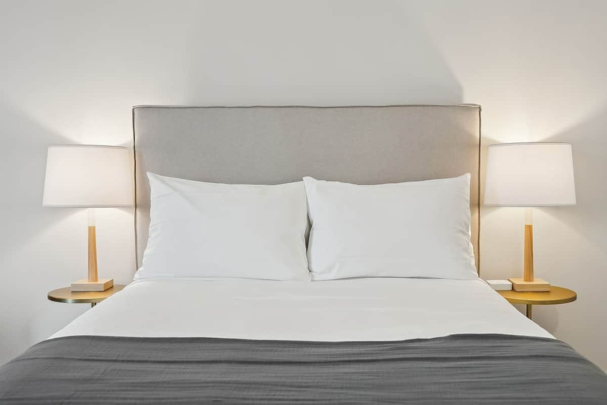 A bed with a grey headboard, white pillows, and a grey bedspread. There are two bedside tables with lamps and books.