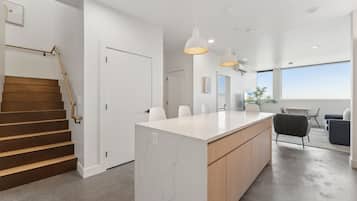 A modern kitchen with a marble island, wooden cabinets, pendant lighting, and a staircase with wooden steps.