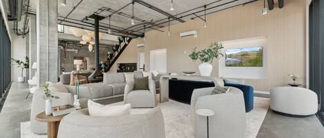 A modern living room with a sofa, armchairs, and a coffee table. There is a staircase in the background leading to another level.