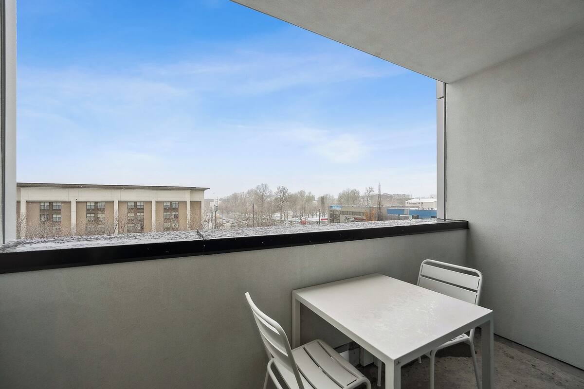 A balcony with a table and chairs, a view of a building, and a snowy landscape.
