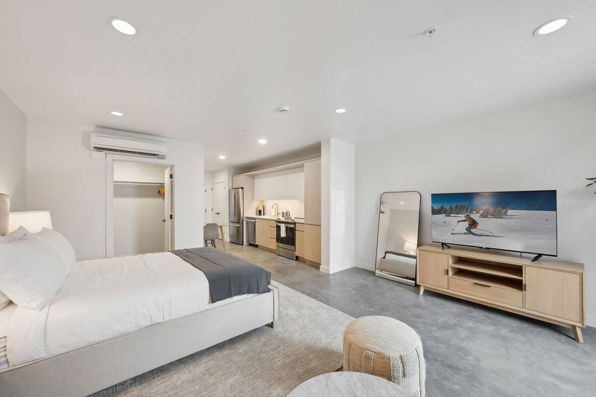A modern hotel room with a bed, a TV, a kitchenette, and a bathroom.