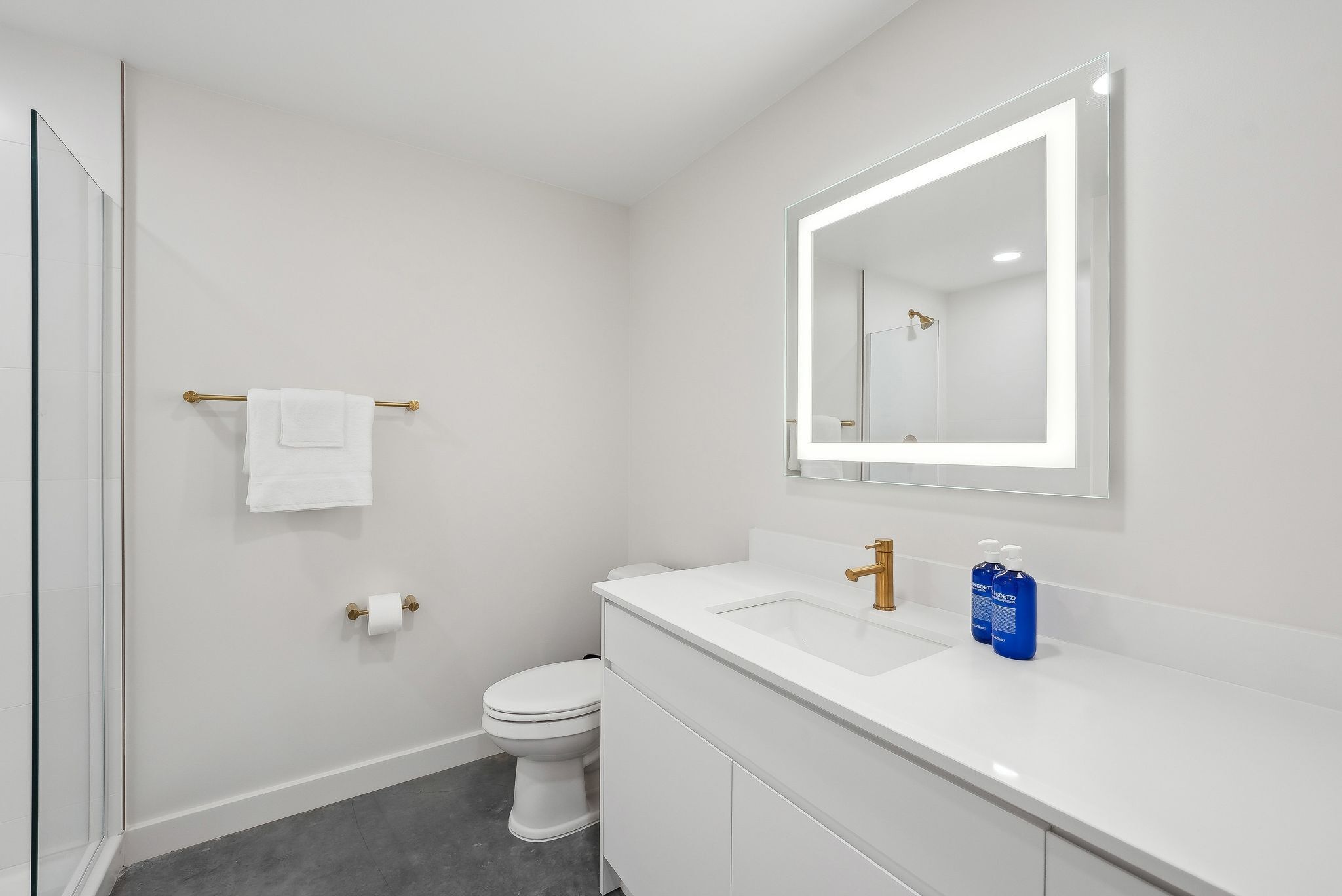 A modern bathroom with a white vanity, a large mirror, and a toilet.