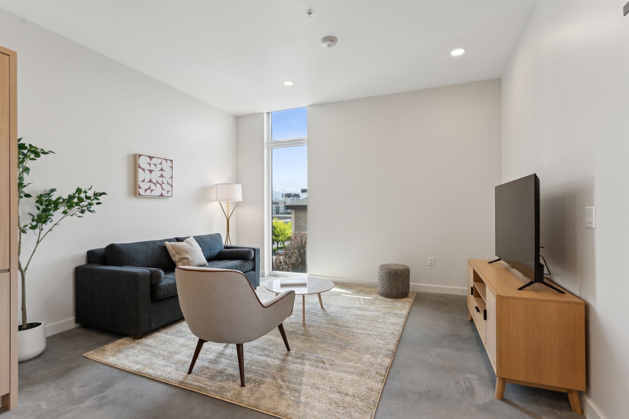 A modern living room with a sofa, armchair, coffee table, TV, and a large window.