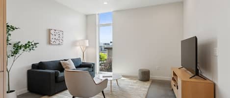 A modern living room with a sofa, armchair, coffee table, TV, and a large window.