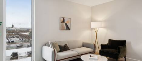 A modern living room with a sofa, armchair, and a coffee table. A floor lamp and a painting are also visible.