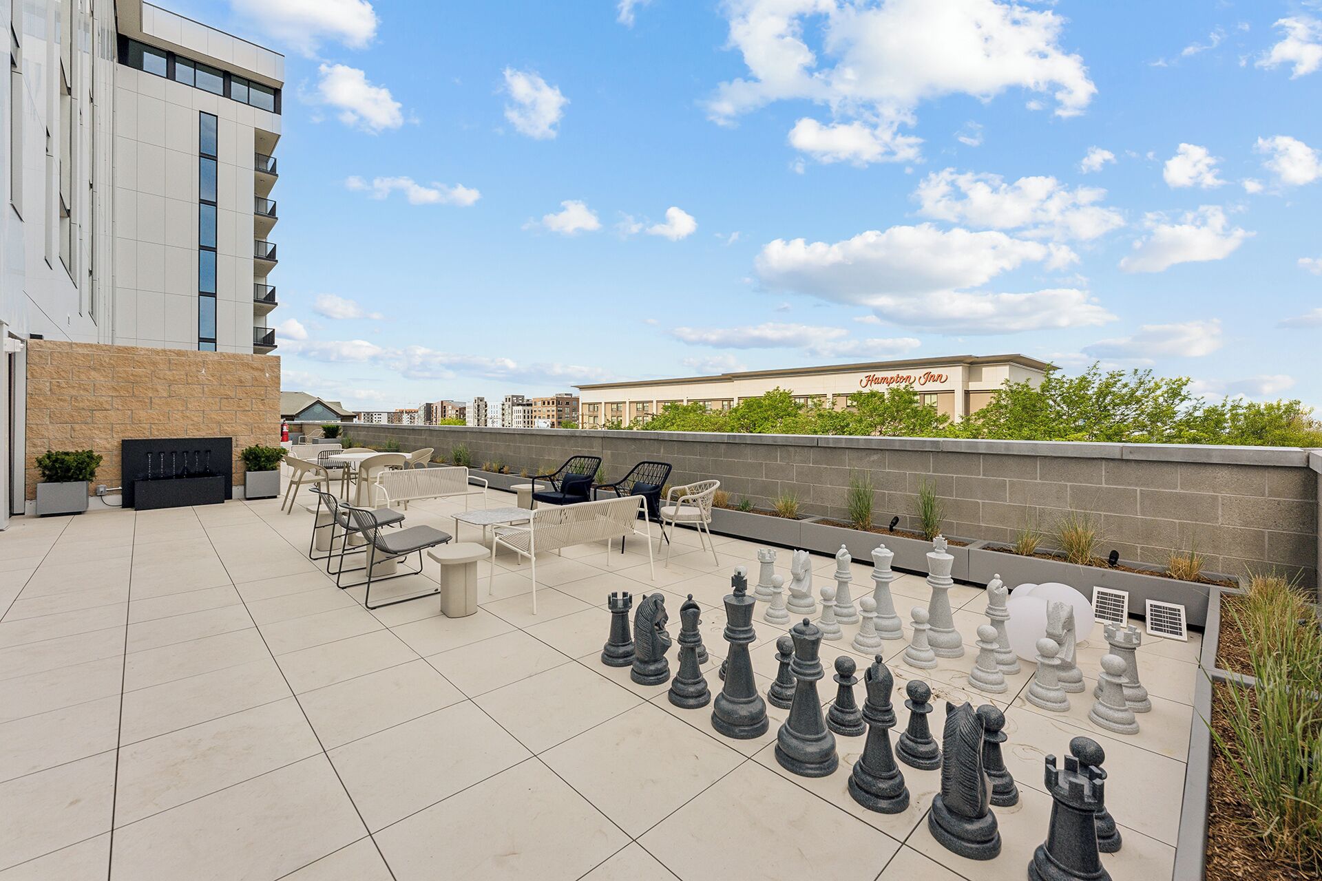 An outdoor seating area with chess pieces arranged on the floor, surrounded by chairs and tables.