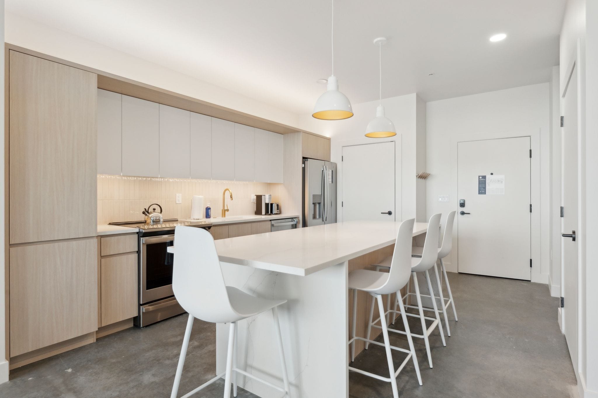 A modern kitchen with white cabinetry, stainless steel appliances, and a central island with bar stools.