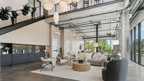 A spacious living area with a high ceiling, exposed ductwork, and a staircase leading to an upper level. -  Placemakr Salt Lake City Downtown, Apartments by Hilton (Salt Lake City)