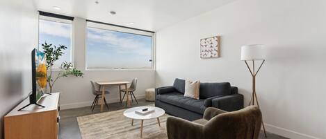 A modern living room with a grey sofa, a round coffee table, a brown armchair, a floor lamp, and a painting on the wall.
