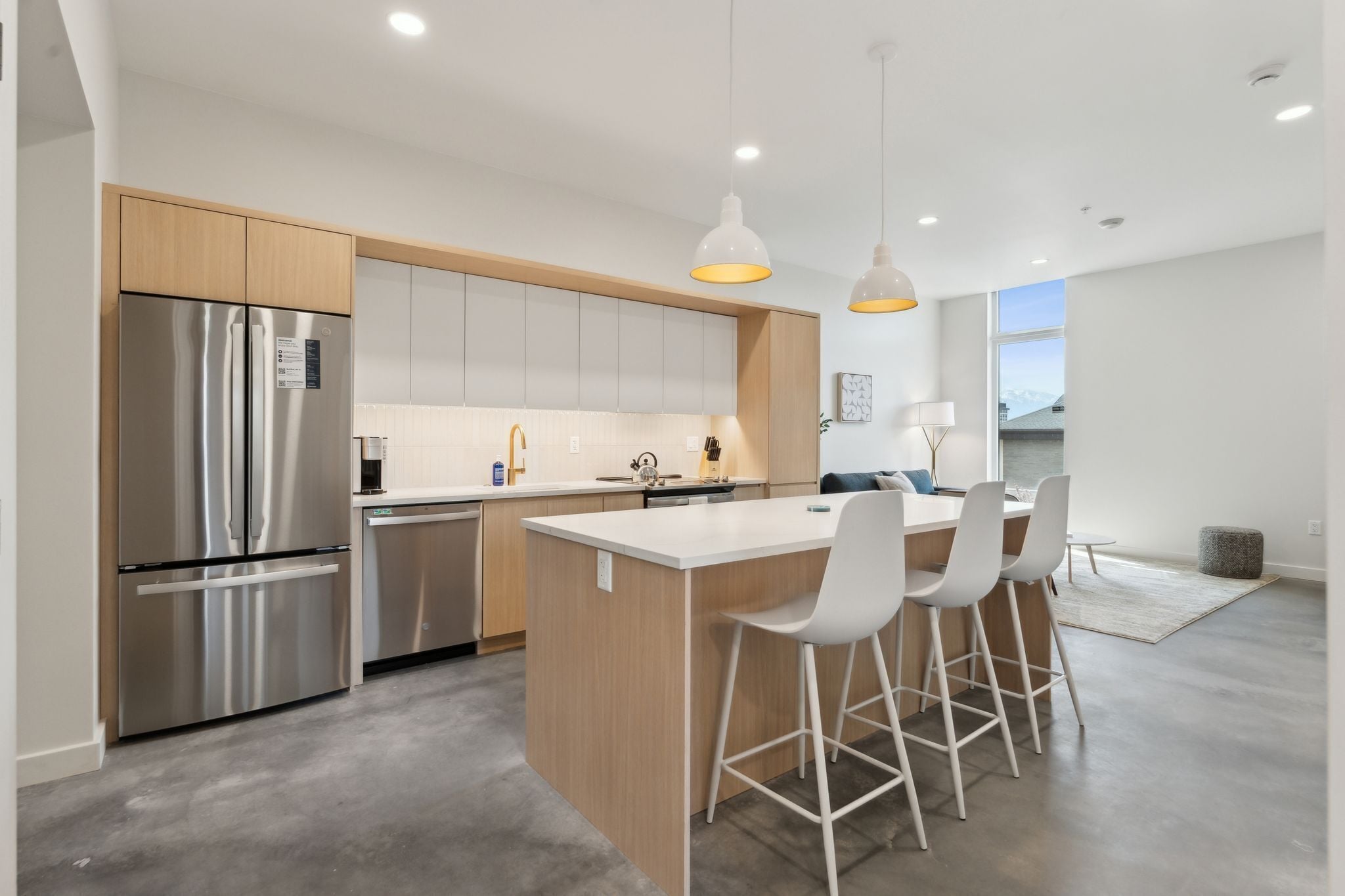 Una cocina moderna con un refrigerador de acero inoxidable, armarios de madera, una isla central con taburetes altos e iluminación colgante.