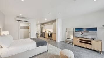 A modern hotel room with a bed, a TV, a kitchenette, and a bathroom.