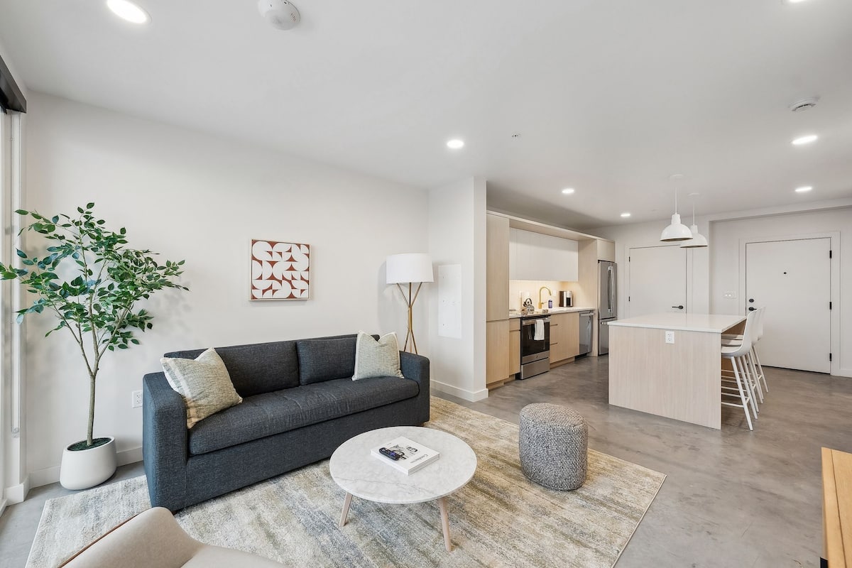 A modern living room with a grey sofa, a round coffee table, and a potted plant.