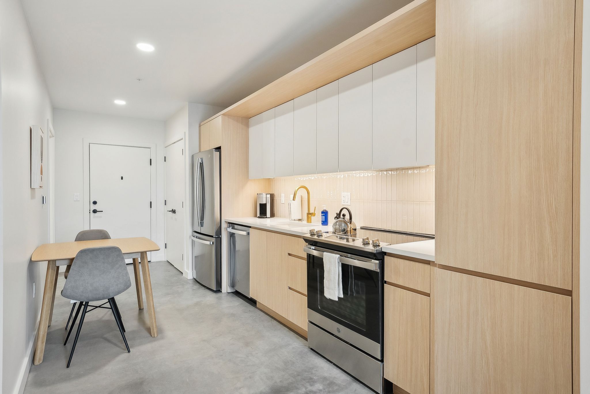 Una cocina moderna con armarios de madera, un refrigerador de acero inoxidable, horno empotrado y una zona de comedor con mesa y sillas.
