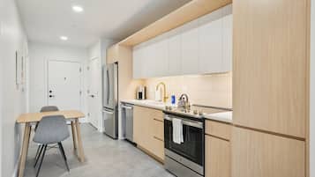 A modern kitchen with wooden cabinets, a stainless steel refrigerator, a built-in oven, and a dining area with a table and chairs.