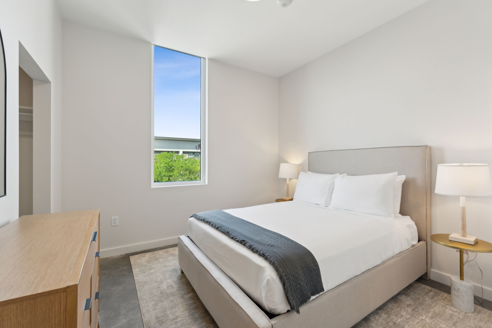 Une chambre d’hôtel moderne avec un grand lit, des lampes de chevet, un bureau en bois et une vue sur la verdure par la fenêtre.