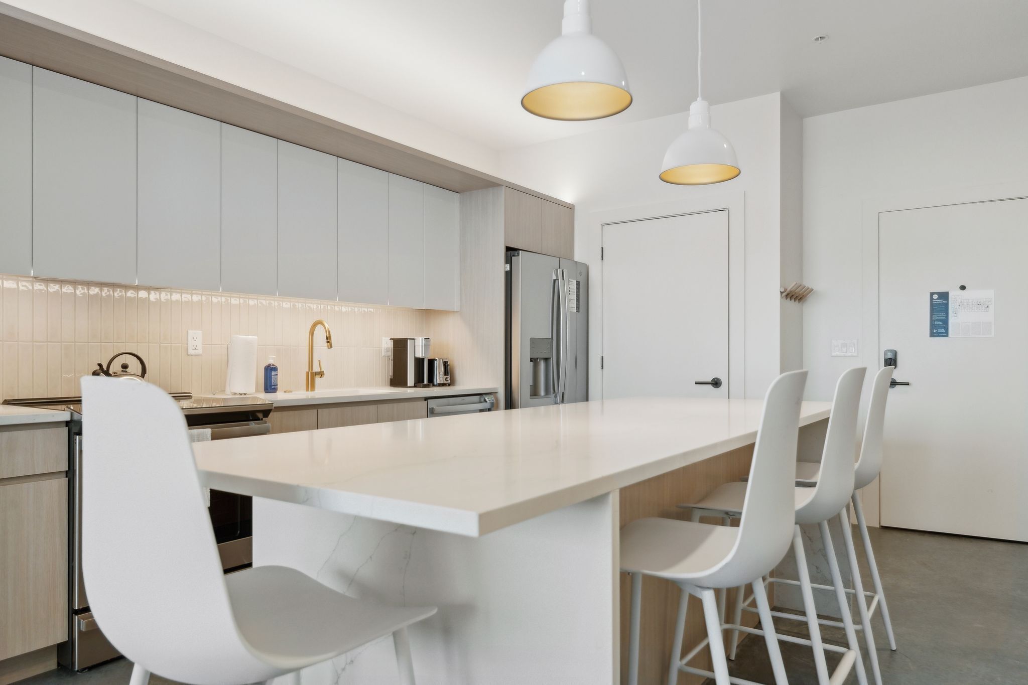 Une cuisine moderne dotée d’un grand îlot central, de tabourets de bar blancs et de luminaires suspendus.
