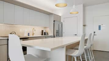 A modern kitchen with a large island, white bar stools, and pendant lighting.