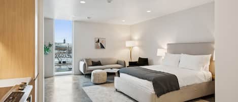 A modern bedroom with a large bed, a sofa, a coffee table, and a view of the city through large windows.