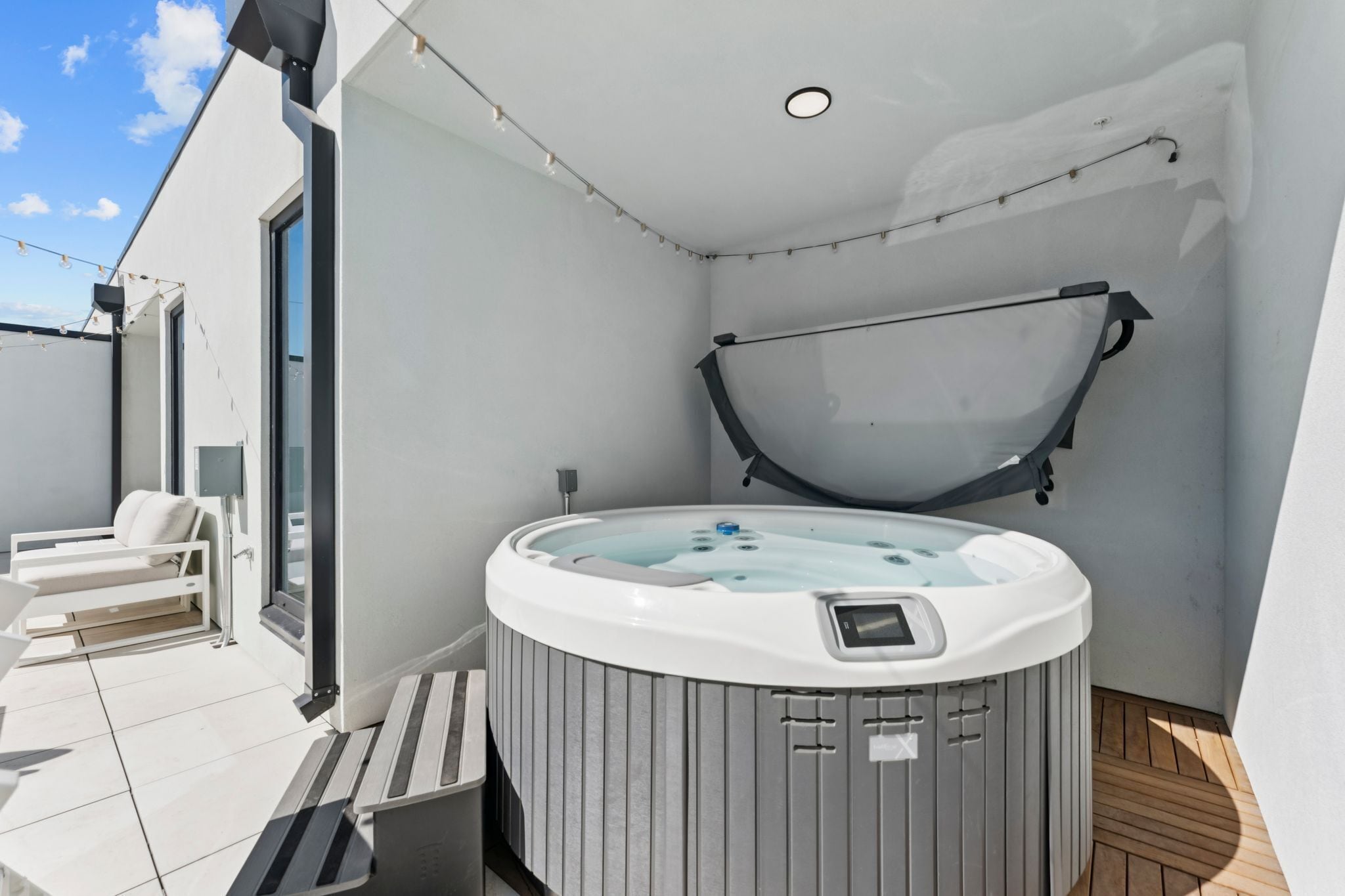 Un moderno espacio al aire libre con jacuzzi, banca y zona de estar cubierta.